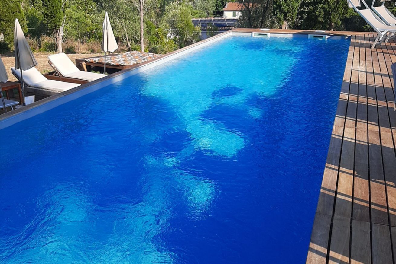Une piscine rectangulaire à l’eau d’un bleu cristallin, entourée d’une terrasse en bois et de chaises longues blanches.