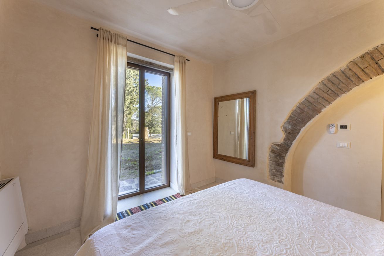 Een slaapkamer met een groot bed, een raam met gordijnen, een spiegel en een boog van baksteen.