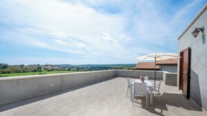 Una terrazza sul tetto con tavolo e sedie, vista sulla campagna e un edificio con tetto in tegole.