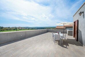 Eine Dachterrasse mit Tisch und Stühlen, Blick auf die Landschaft und ein Gebäude mit Ziegeldach.