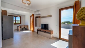 Un soggiorno moderno con una televisione a schermo piatto, una zona pranzo con tavolo e sedie, e una cucina con frigorifero.