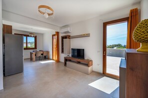 Ein modernes Wohnzimmer mit Flachbildfernseher, einem Essbereich mit Tisch und Stühlen sowie einer Küche mit Kühlschrank.