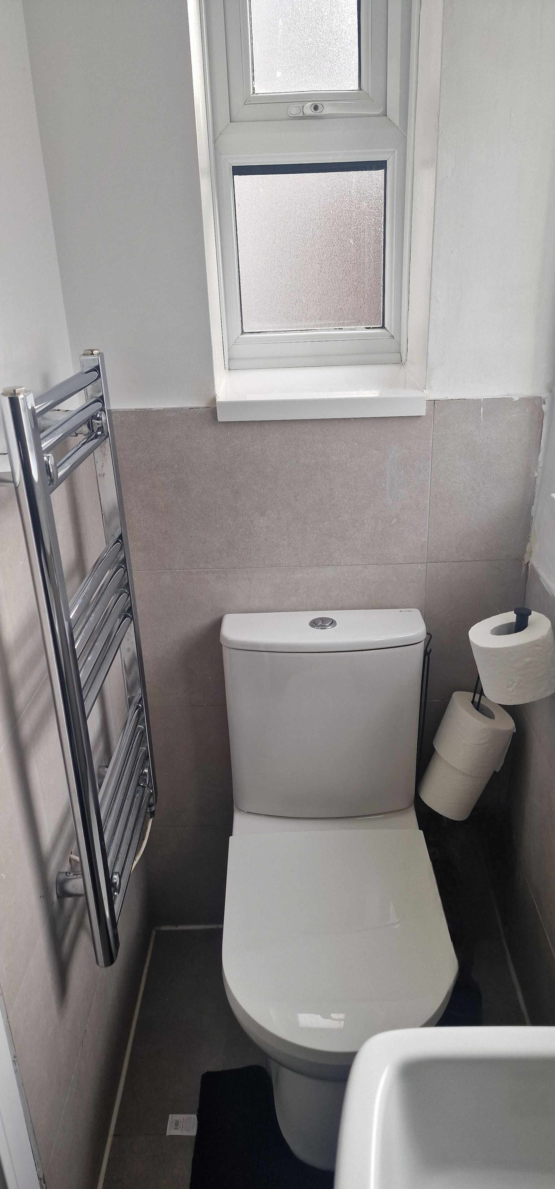 A small bathroom with a white toilet, a towel rack, and a window above the toilet.