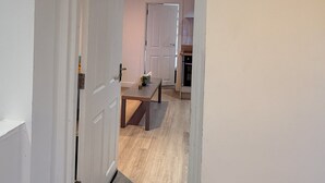 A hallway leading to a kitchen with a wooden floor and white walls. - Cozy 1 Bedroom Fully Furnished Apartment (Leicester)