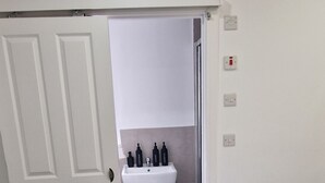 A bedroom with a bed, a white door, a bathroom with a sink and toiletries, and a window. - Cozy 1 Bedroom Fully Furnished Apartment (Leicester)