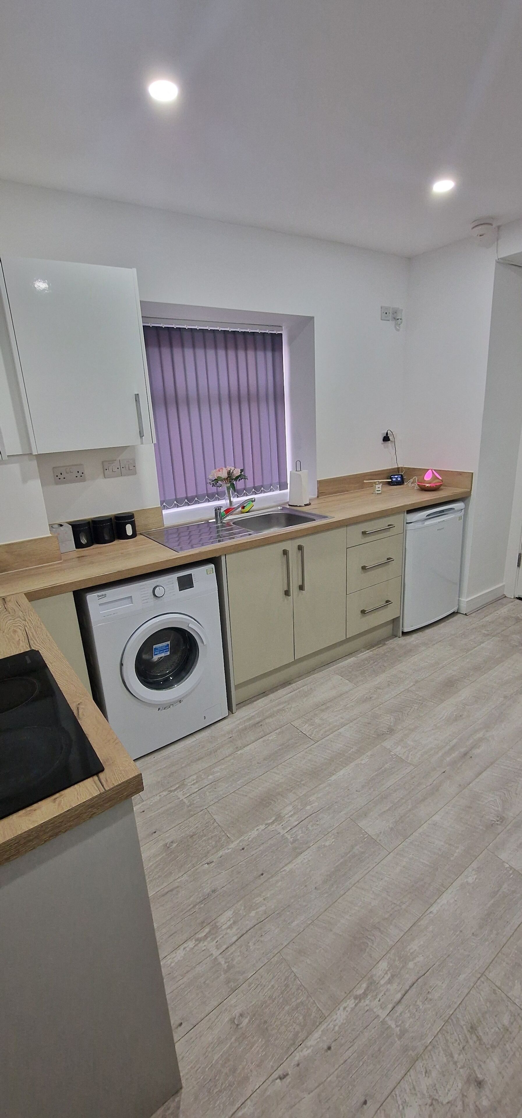 Una cocina moderna con lavadora, encimera de madera y una ventana con cortinas moradas.