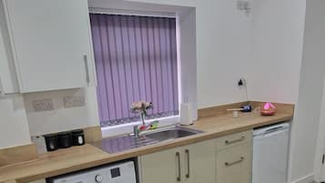 Una cocina moderna con lavadora, encimera de madera y una ventana con cortinas moradas.