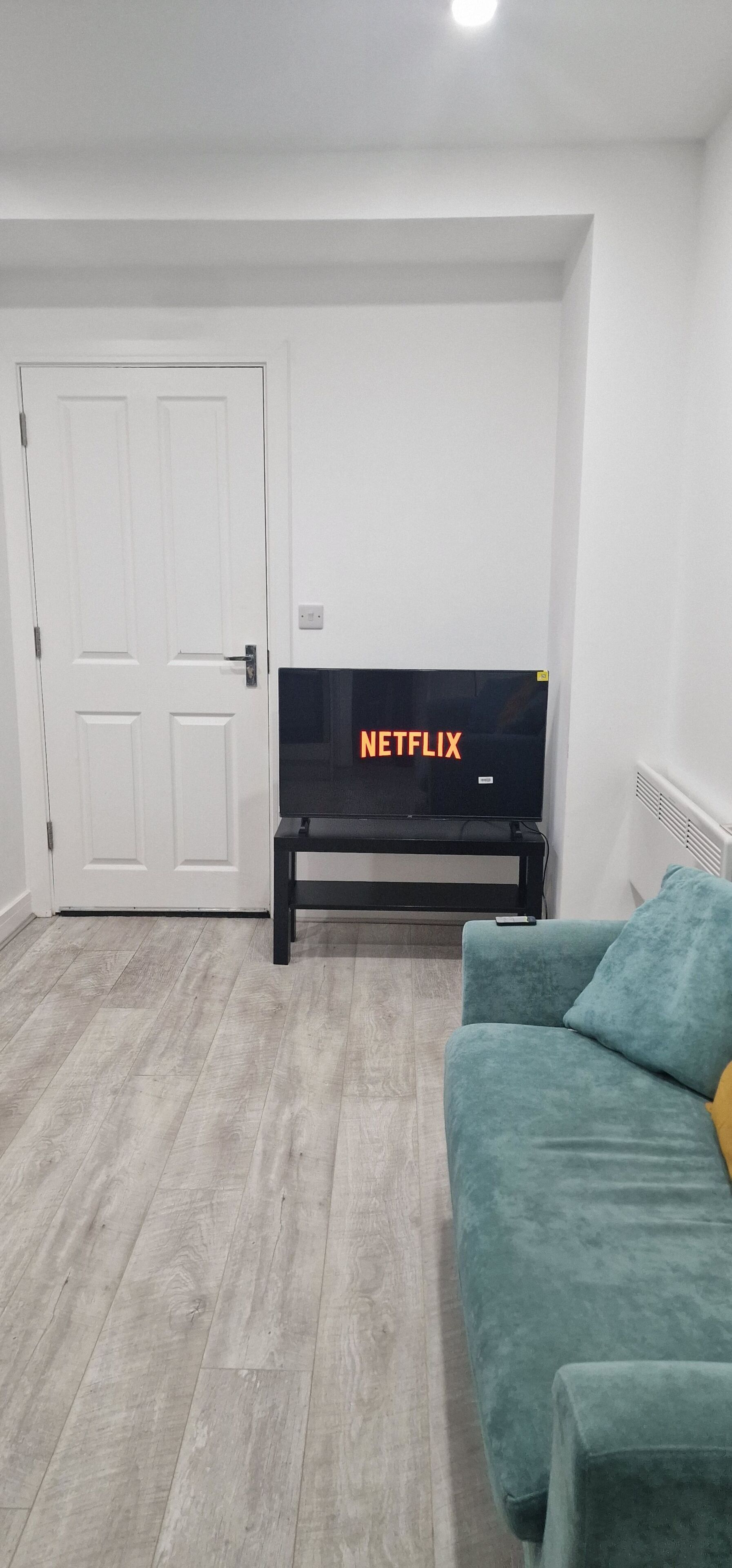 A living room with a black TV on a stand, a teal sofa, and a white door.