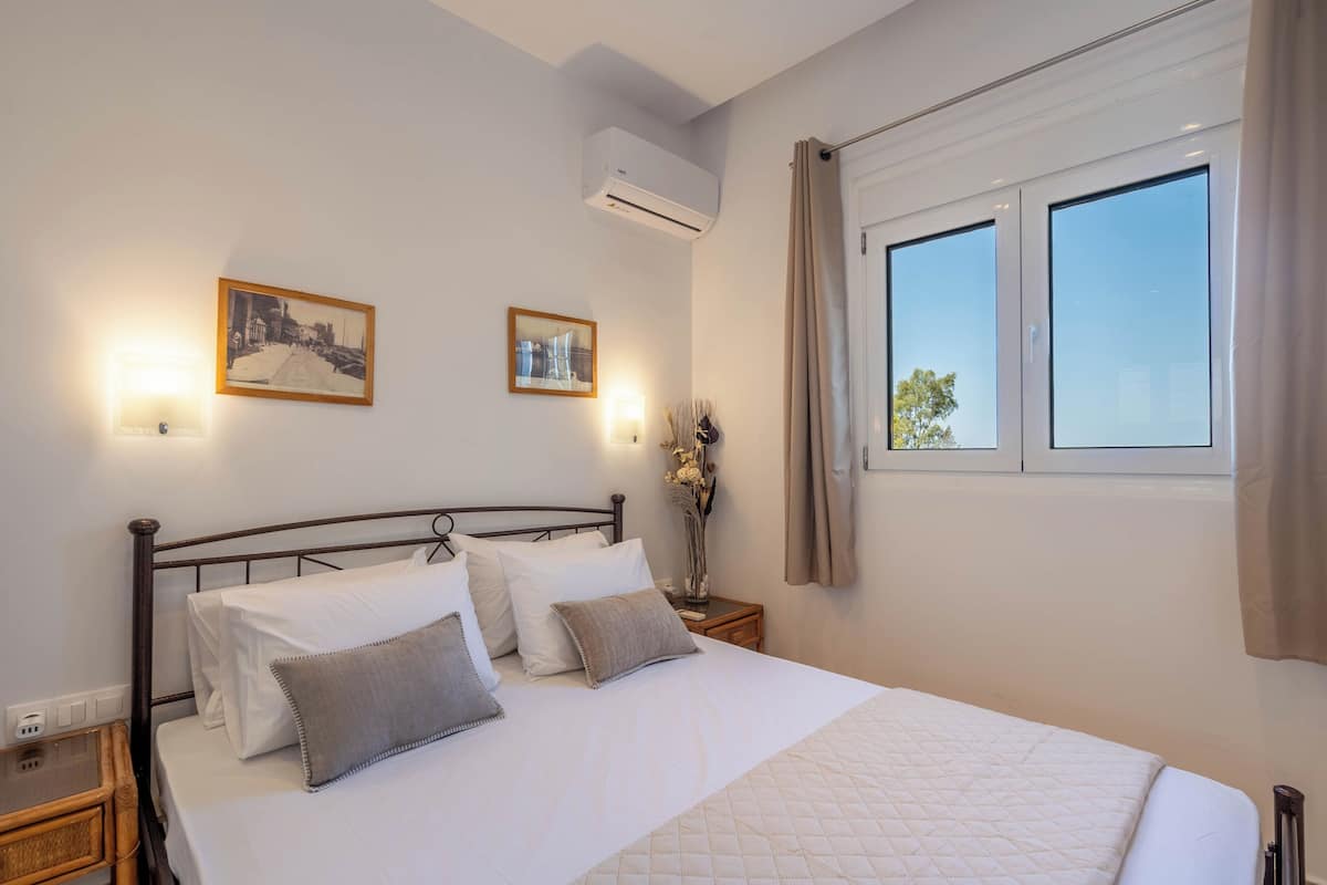 A neatly made bed with white linens and a quilted cover, a bedside table with a lamp, and two framed pictures on the wall.