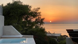 Vista al atardecer desde un balcón con piscina, que da a una masa de agua y tierra lejana.
