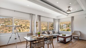 Una habitación amplia con una mesa de comedor, sillas, un sofá y una butaca. Un telescopio está apoyado contra la pared.