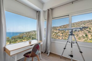 Ein Zimmer mit Schreibtisch und Stuhl, einem Teleskop und großen Fenstern mit Blick auf das Meer und die Hügel.