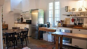 A kitchen with a stainless steel refrigerator, wooden table, chairs, and a coffee maker. - Historic 4BR Village Home | Terrace | Beach 15 min (Ollioules)