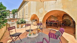 An outdoor patio with a table set for dining, surrounded by arches and a view of the city. - Historic 4BR Village Home | Terrace | Beach 15 min (Ollioules)