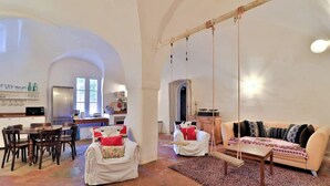 A spacious living area with a swing, a dining table with chairs, and a kitchen in the background. - Historic 4BR Village Home | Terrace | Beach 15 min (Ollioules)