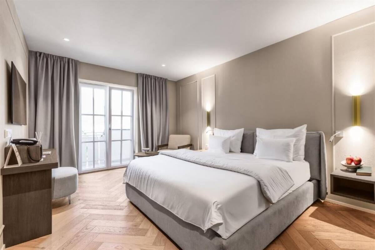 Een moderne slaapkamer met een groot bed, een bureau en een stoel. Er is een raam met gordijnen en uitzicht op de omgeving.