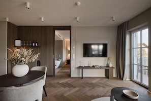 Un salon moderne comprenant un coin repas, un téléviseur à écran plat fixé au mur et une vue sur l’extérieur grâce à de grandes fenêtres.