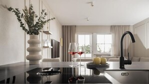 A modern kitchen with a black countertop, a vase with dried flowers, two wine glasses, and a bowl of apples. - Lingers Suites & Residence (Appiano Sulla Strada del Vino)