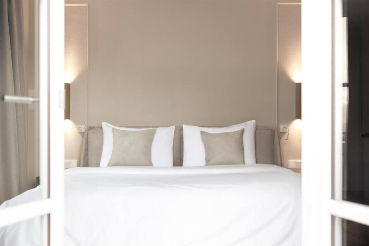 Een net opgemaakt bed met witte lakens en twee kussens, in een kamer met een neutrale kleurenstelling en minimalistische inrichting.