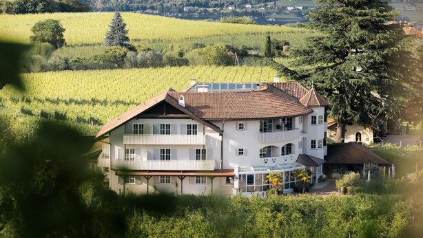 A multi-story building with a sloped roof, surrounded by lush greenery and vineyards. - Lingers Suites & Residence (Appiano Sulla Strada del Vino)
