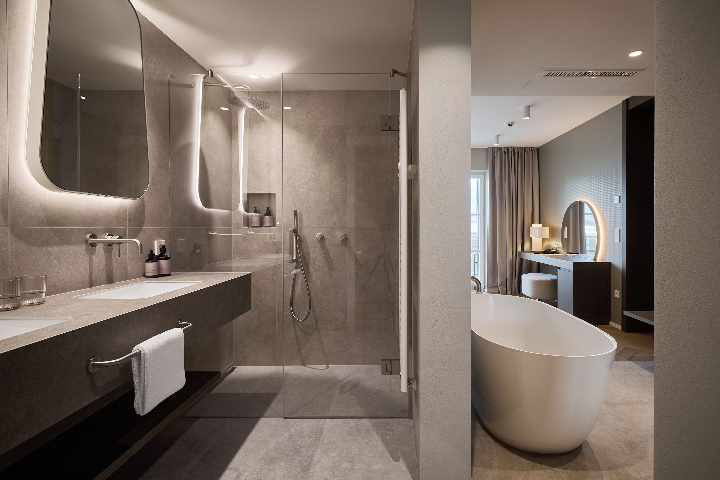 Ein modernes Badezimmer mit bodengleicher Dusche, einer großen Badewanne und einem Waschtisch mit Spiegel.