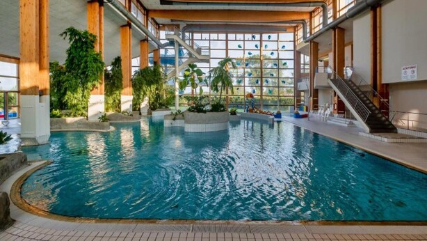 An indoor swimming pool with a view of a cityscape through large windows. - Sunday Resort Rugen Manor Suite (Sagard)