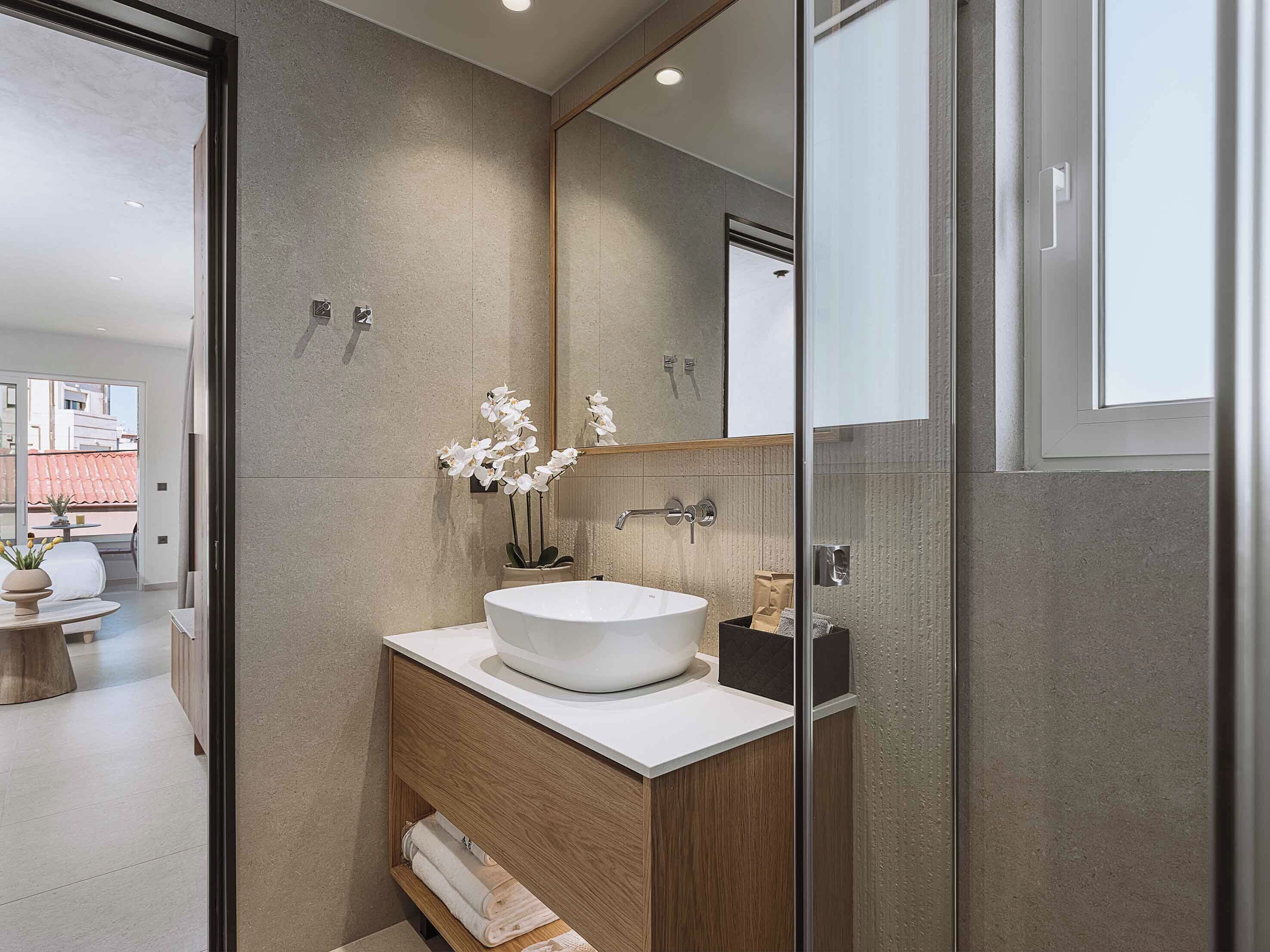 A modern bathroom with a large mirror, a white sink, and a wooden vanity.