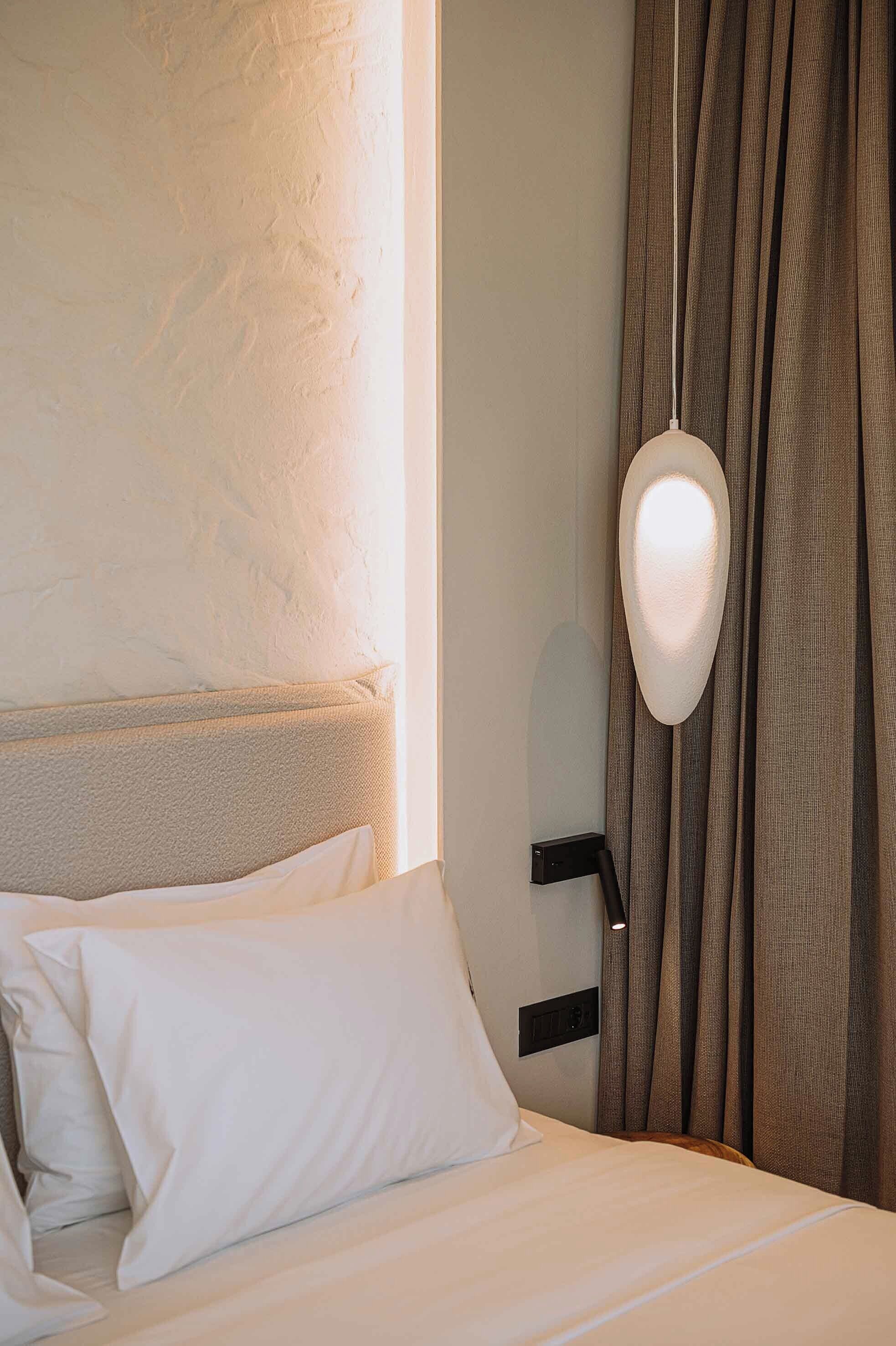 Une chambre d’hôtel avec un lit, une tête de lit, une lampe fixée au mur et des rideaux.
