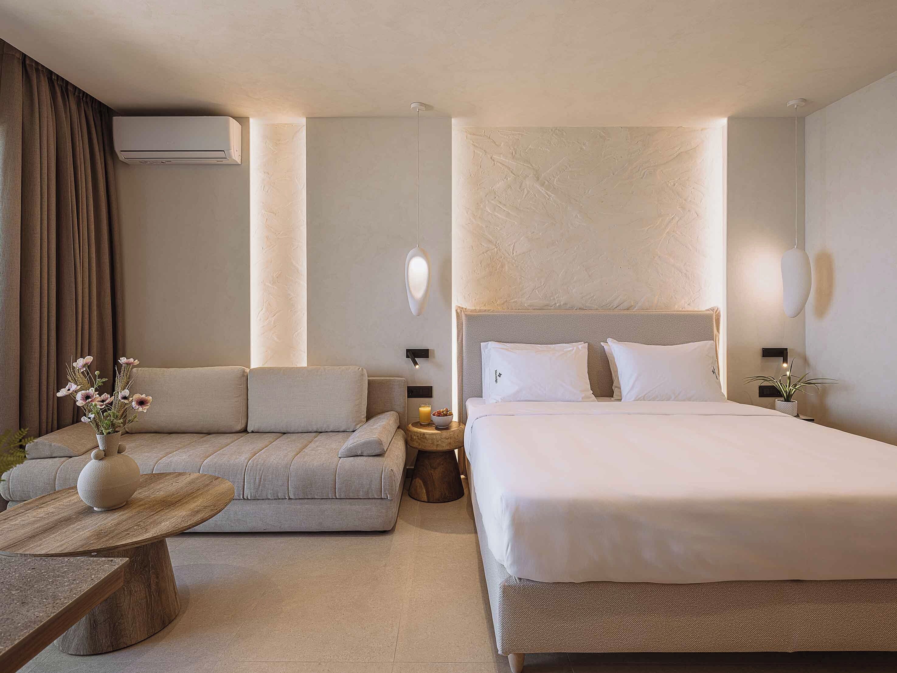 A hotel room with a bed, a sofa, a small round table, and an air conditioning unit.
