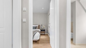 Un pasillo que conduce a un dormitorio con cama, mesita de noche y velador.