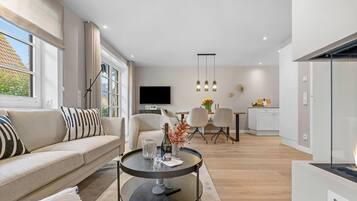 Una sala de estar moderna con un sofá, una mesa redonda de centro, un televisor y un comedor con sillas y una mesa.