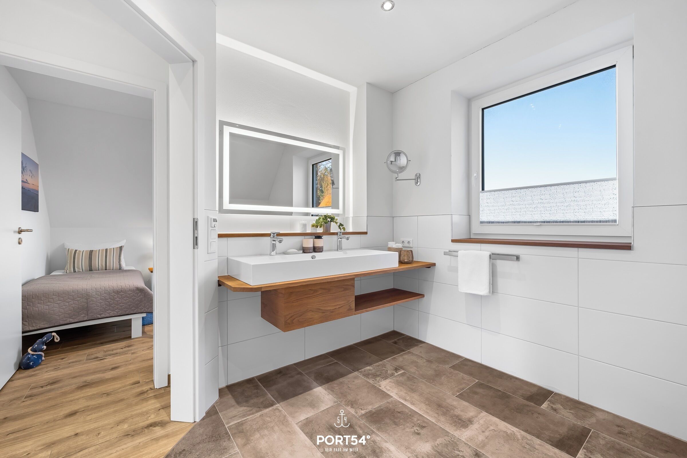 A modern bathroom with a large mirror, wooden vanity, and a view of the sea through a window.