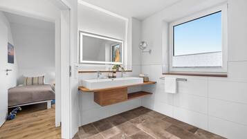 A modern bathroom with a large mirror, wooden vanity, and a view of the sea through a window.