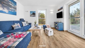 A modern living room with a blue sofa, a coffee table, and a large window. - High-quality holiday home in Sankt Peter-Ording with garden (Sankt Peter-Ording)