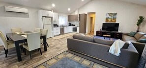 A modern apartment with a dining area, sofa, TV, kitchen, and a painting on the wall. - The Long Jetty Beach House (Port Welshpool)