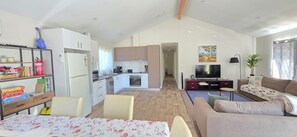 A modern apartment with a dining area, kitchen, living room, and a TV. - The Long Jetty Beach House (Port Welshpool)