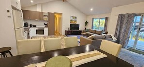 A modern living room with a sofa, a dining table, and a kitchen area with cabinets and appliances. - The Long Jetty Beach House (Port Welshpool)