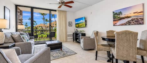 A modern living room with a balcony, a ceiling fan, a flat-screen TV, and a dining area with chairs and a table.