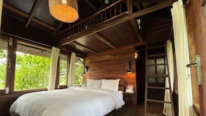 A wooden cabin bedroom with a large bed, a ladder, and a window overlooking greenery. - Landmark Farmhouse (Bharatpur)