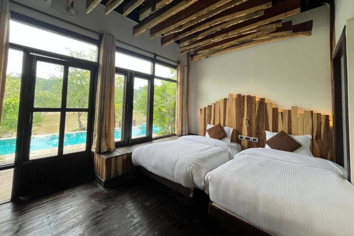 A hotel room with two beds, large windows, a wooden ceiling, and a view of a swimming pool.