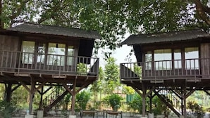 Two wooden cabins with balconies, surrounded by a garden with rocks and plants. - Landmark Farmhouse (Bharatpur)