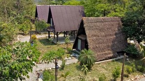 A thatched-roof structure with a flat roof, surrounded by lush greenery and trees. - Landmark Farmhouse (Bharatpur)