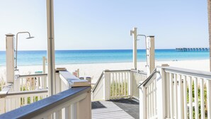 Vistes a la platja des d'un tramat de fusta amb baranes, un moll a la distància i un cel serè.