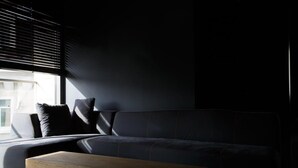 Ein modernes Wohnzimmer mit einem dunkelgrauen Sofa, einem Holztisch und einem Fenster mit Jalousien.