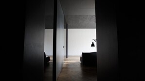 Ein schwach beleuchteter Flur mit Holzboden, einer schwarzen Couch und einer hängenden Pendelleuchte.