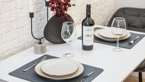 A dining table set with plates, cutlery, and wine glasses, with a bottle of wine and a vase with red flowers in the background. - Modern&Central | WiFi, Coffee, Netflix | GrandStay (Chișinău)