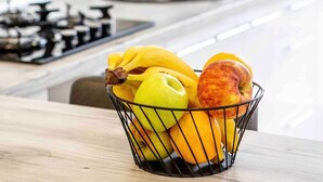 A kitchen with a fruit basket containing bananas, apples, and oranges on the counter. - Modern&Central | WiFi, Coffee, Netflix | GrandStay (Chișinău)