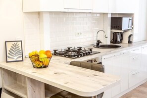 Una cucina moderna con mobili bianchi, un piano di lavoro in legno, un fornello a gas, un lavello e un forno a microonde.