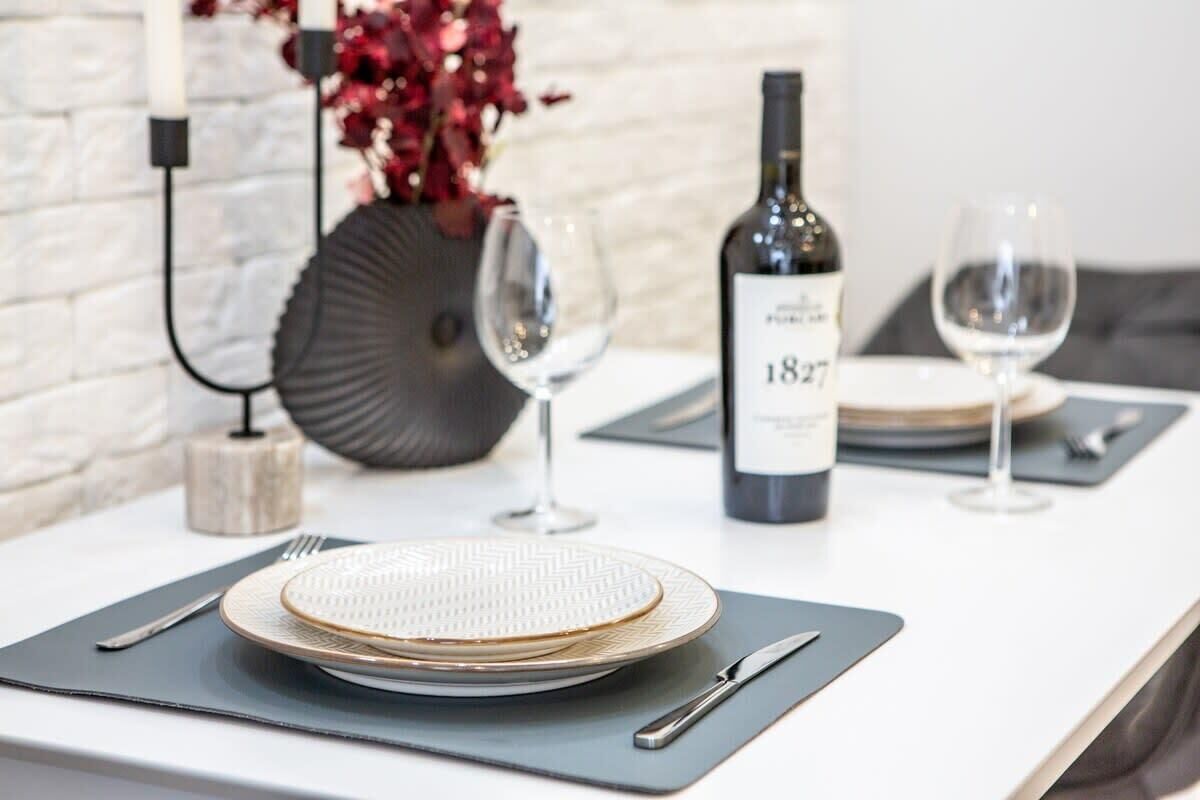 A neatly set dining table with plates, cutlery, and a bottle of wine, suggesting a formal dining experience.