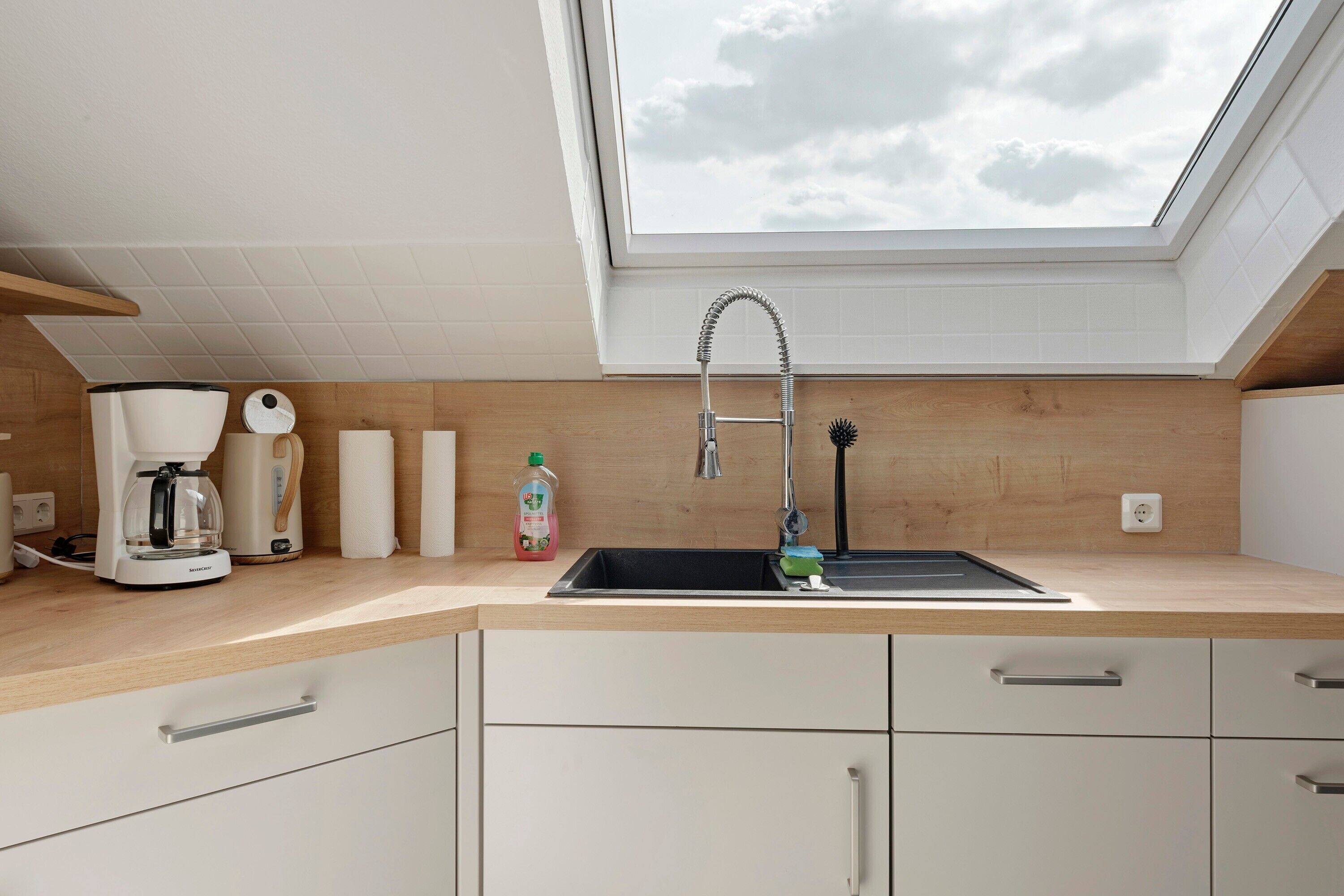 A kitchen with a skylight, a coffee maker, a sink, and a dish soap bottle.